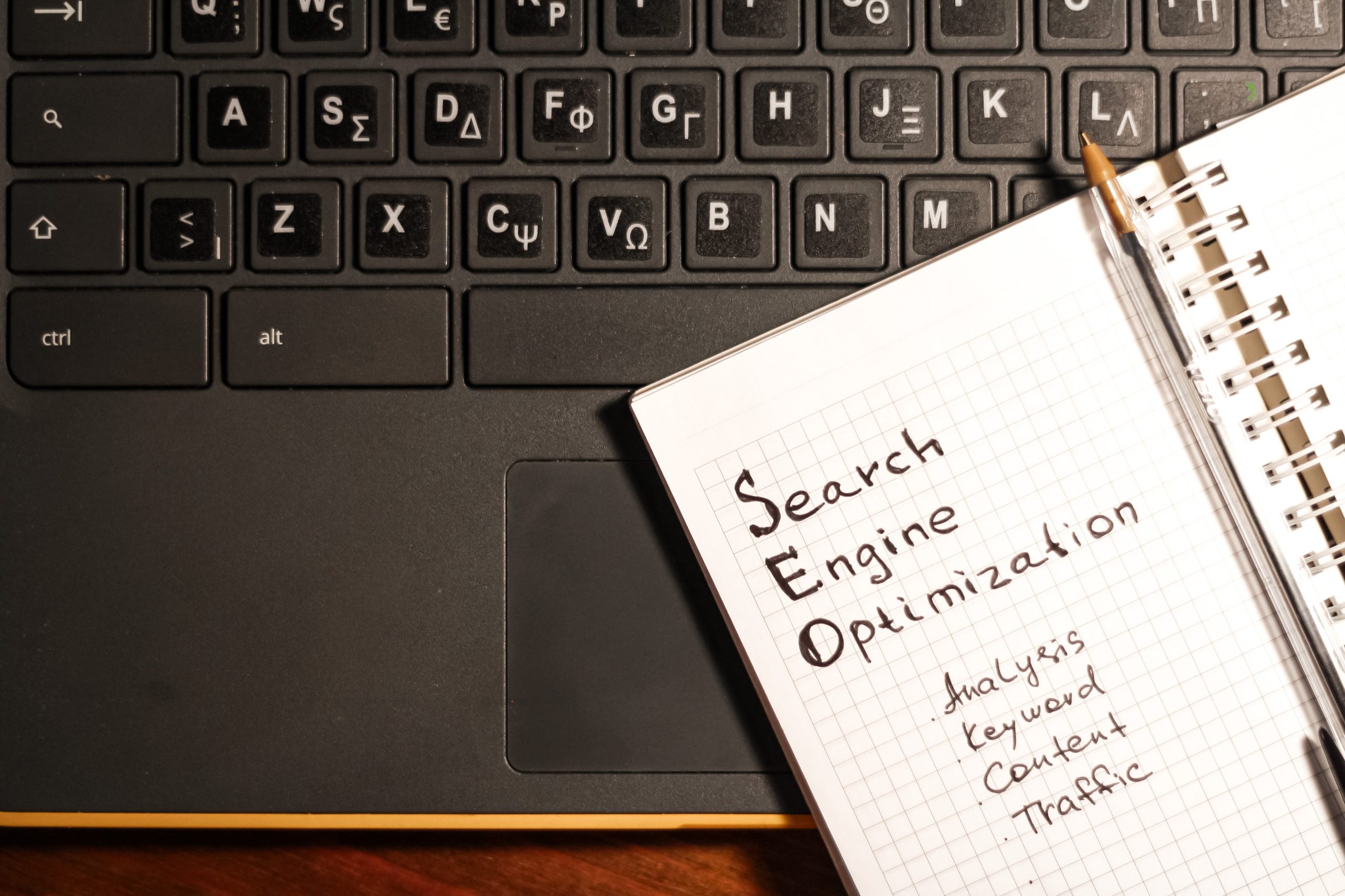 Imagen de un teclado de computadora con una libreta abierta que muestra las palabras Search Engine Optimization, representando una guía completa de SEO para WordPress.