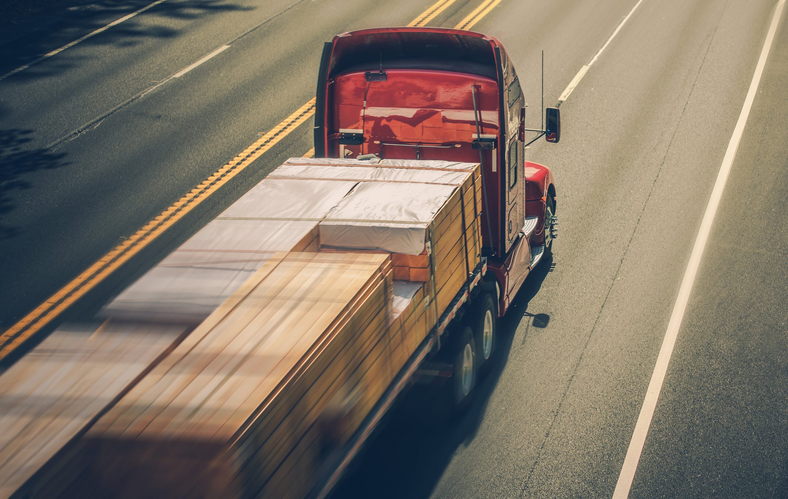 Camión de carga transportando materiales de madera a alta velocidad por una carretera, simbolizando la importancia de la optimización de la velocidad de carga de un sitio web.