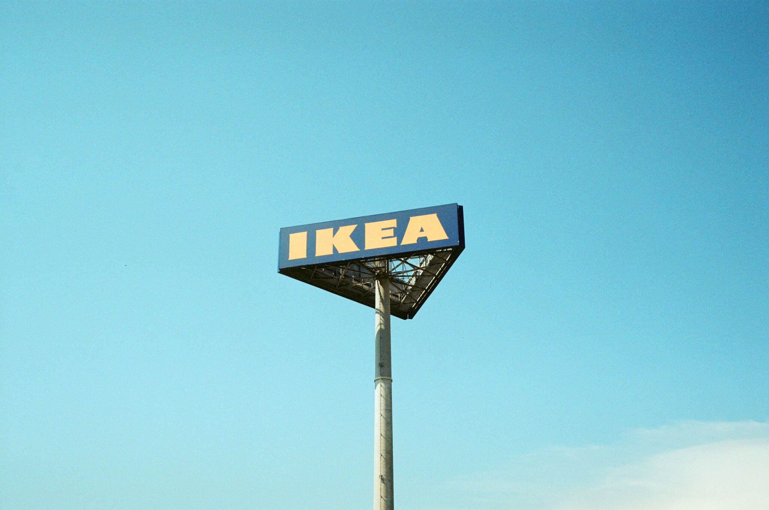 Letrero corporativo azul y amarillo de IKEA montado sobre un poste metálico alto contra un cielo azul despejado.