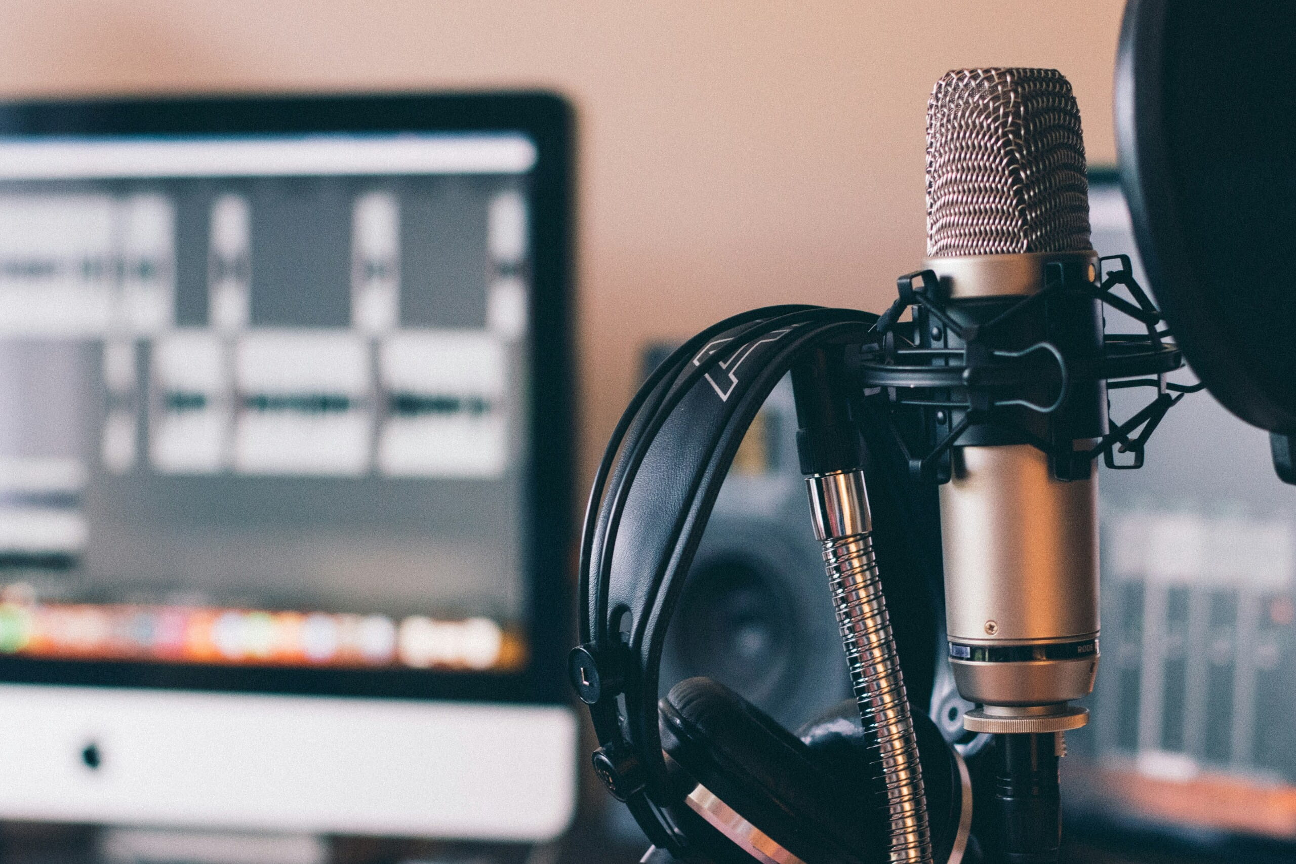Herramientas para la publicidad en podcasts micrófono y producción de audio Micrófono de estudio con auriculares frente a una pantalla de edición, ideal para ilustrar herramientas para la publicidad en podcasts y la creación de contenido de audio.