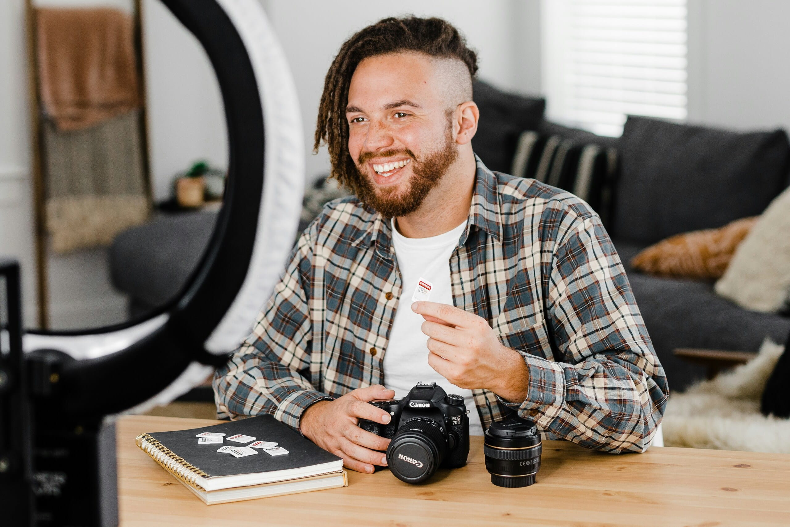 Hombre sonriente con camisa de cuadros sosteniendo una tarjeta de memoria cerca de una cámara Canon sobre una mesa de madera.