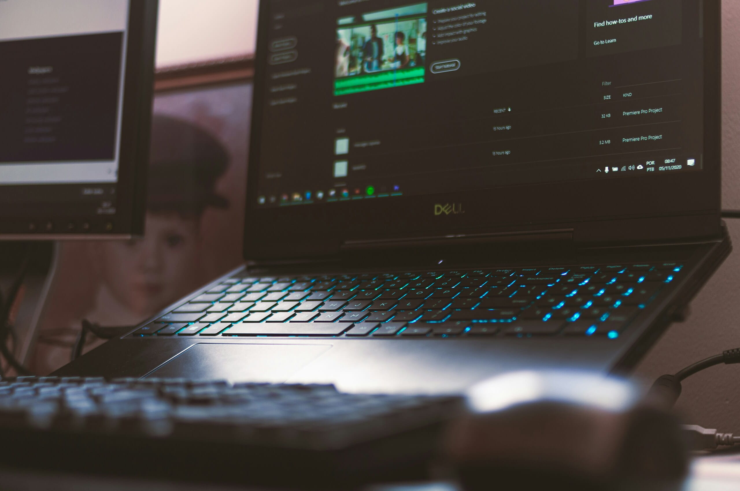 Laptop Dell abierta sobre escritorio con teclado azul brillante y pantalla mostrando interfaz de edición de video Adobe Premiere.