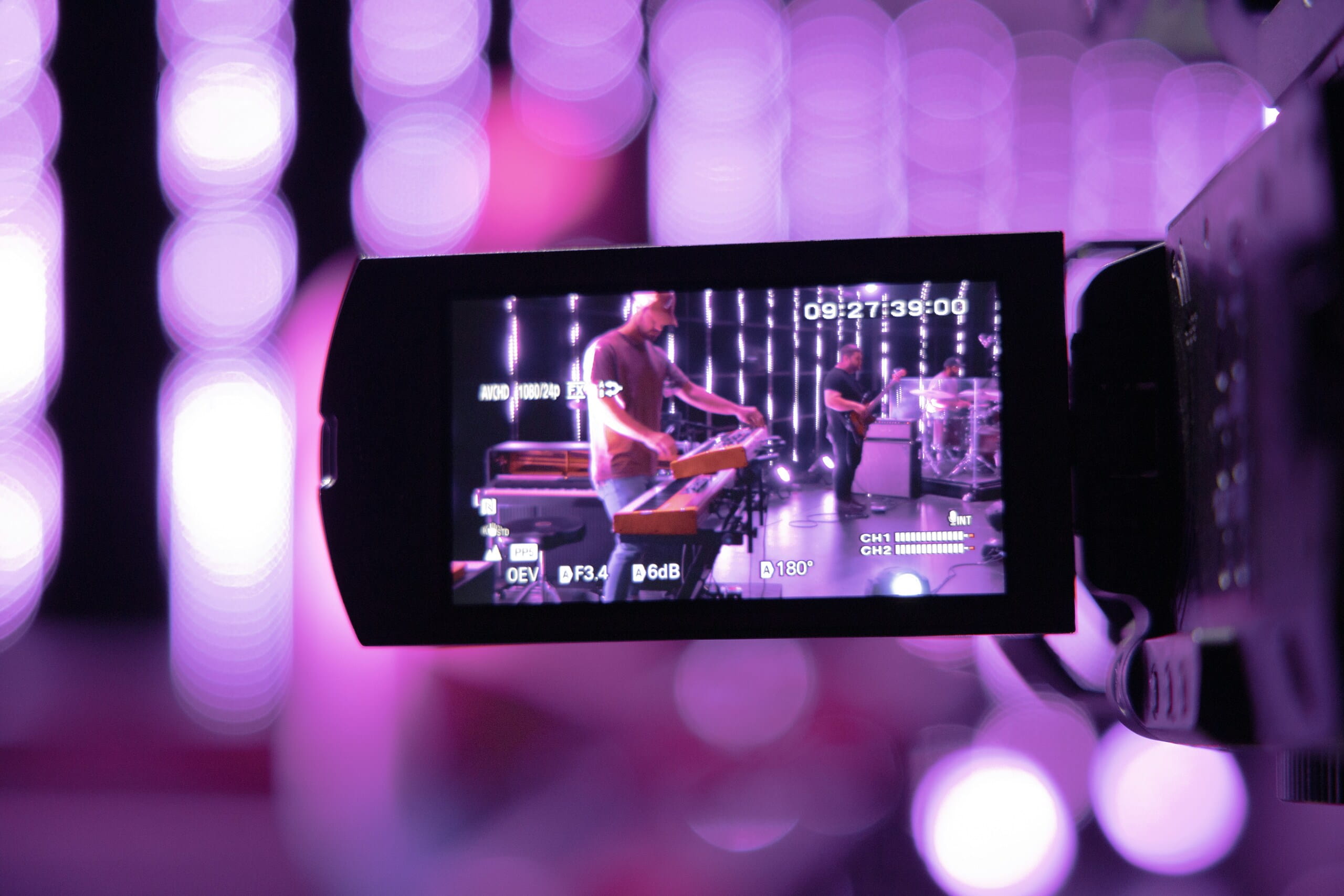 Pantalla LCD de cámara de video mostrando a una banda tocando en un escenario iluminado con luces moradas de fondo.