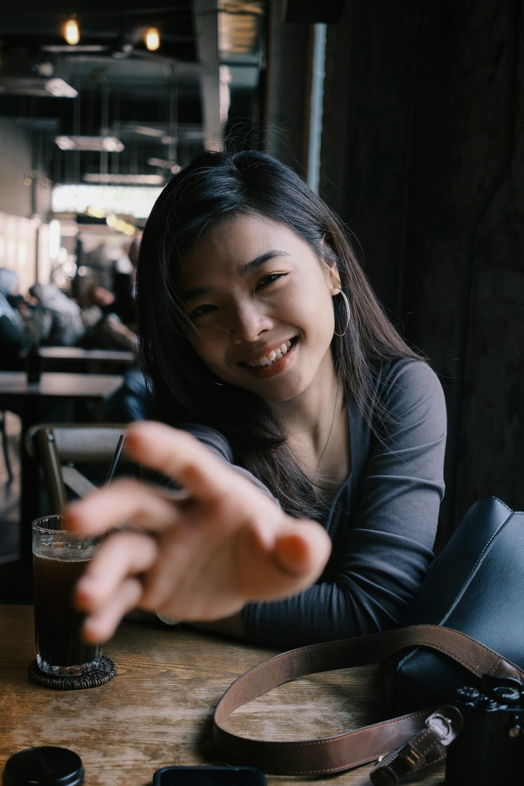 Mujer sonriente en una cafetería, acercando la mano a cámara; ideal para Estrategias para promover contenido viral.
