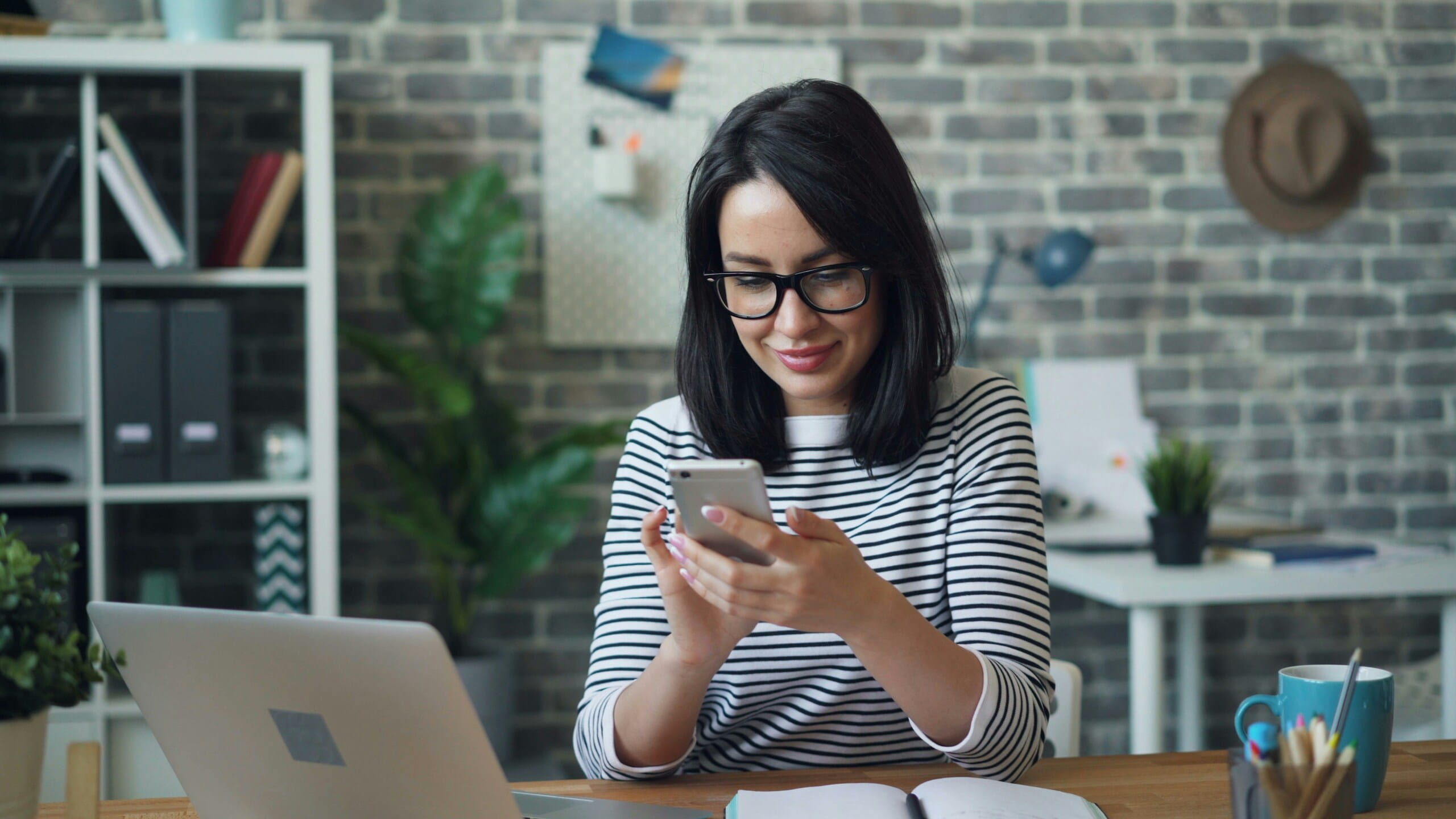 Mujer usando el móvil junto al portátil para gestionar su Perfil de empresa de Google y revisar datos de negocio.