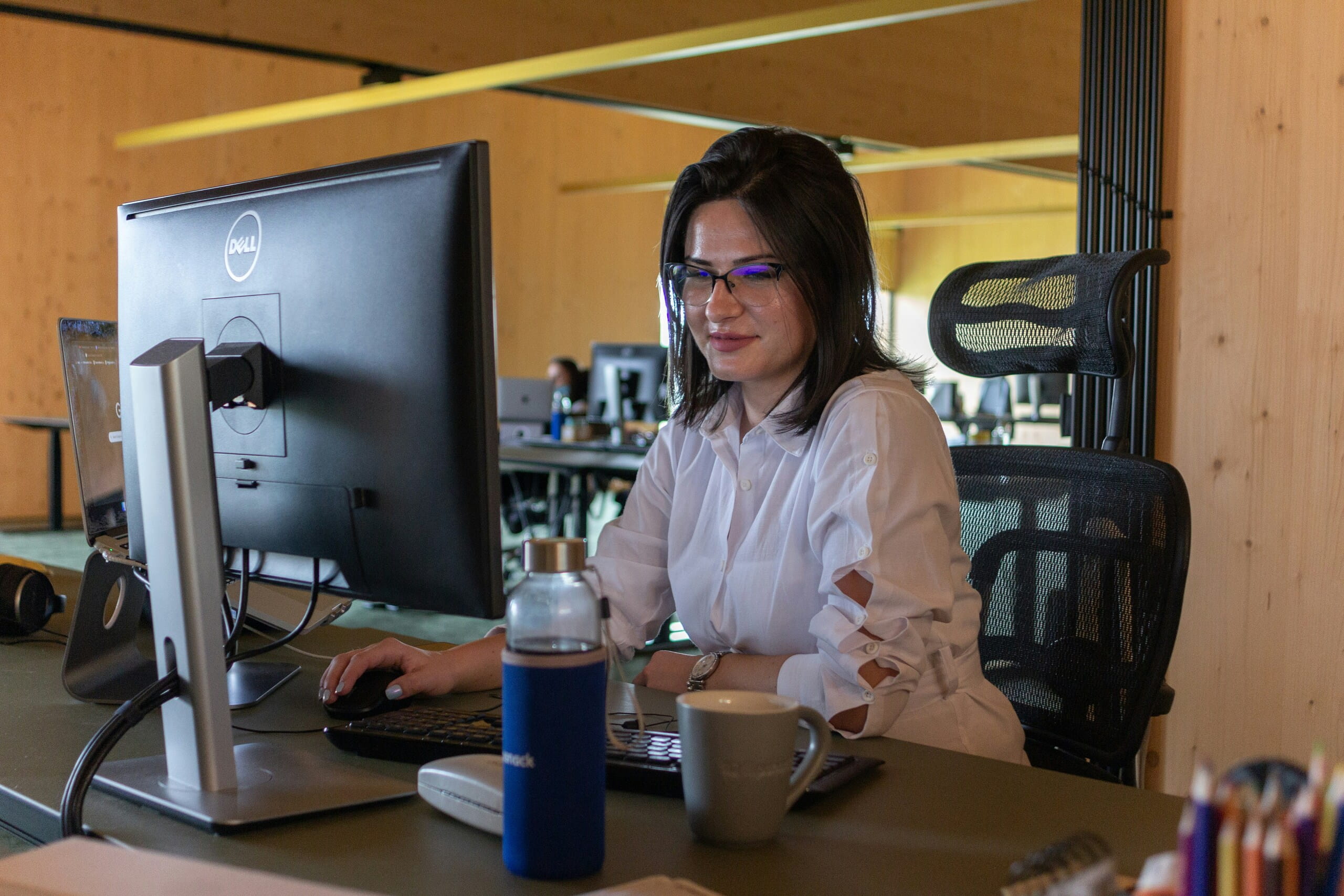 Mujer profesional con gafas trabajando concentrada frente a un monitor Dell en un espacio de oficina moderno.
