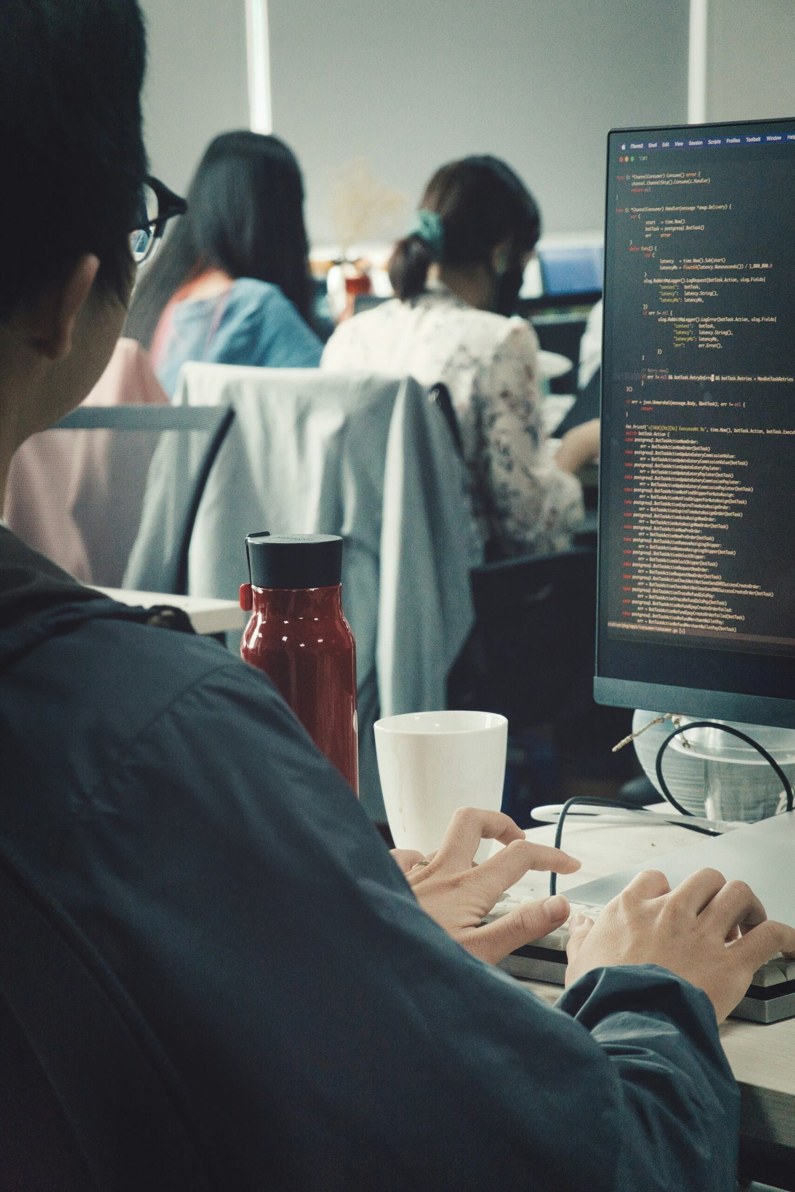 Primer plano de unas manos tecleando código en un teclado, con líneas de código de programación en la pantalla.