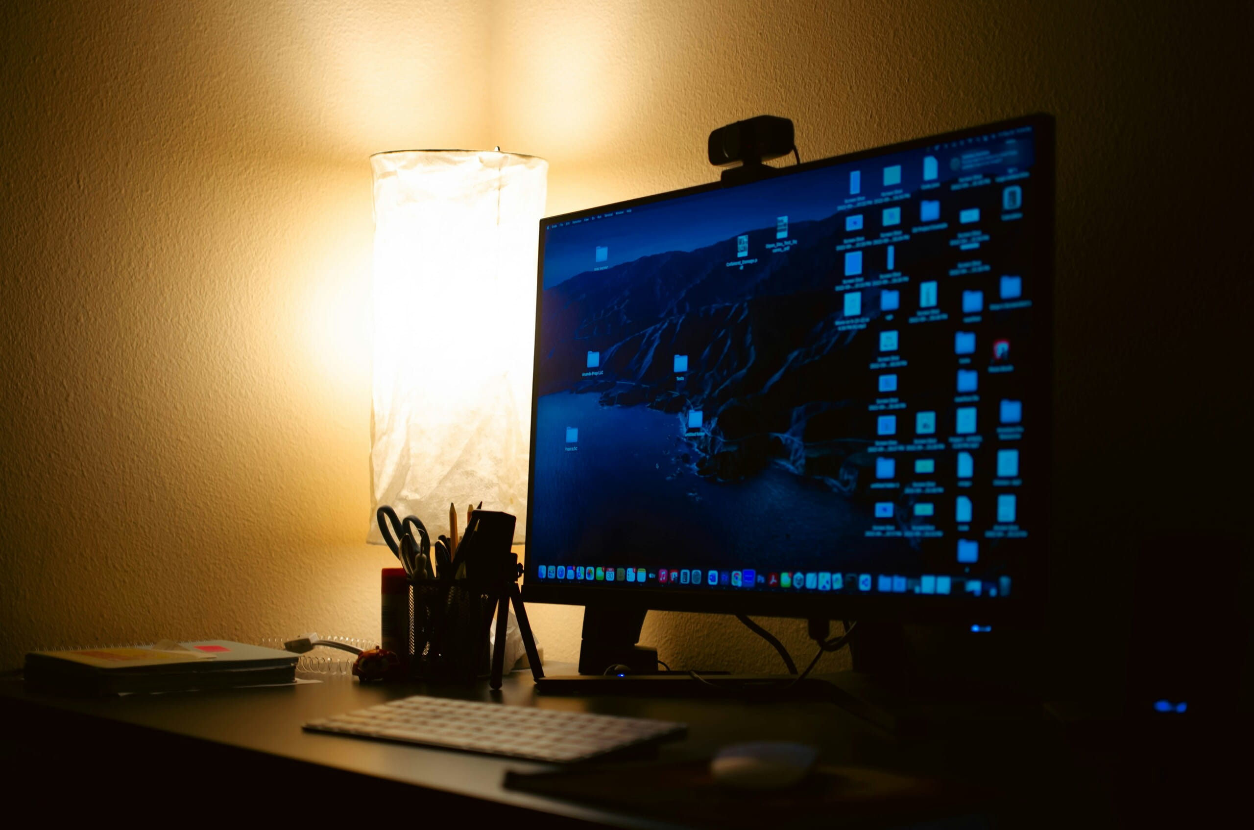 Escritorio moderno para oficina en casa con monitor digital, teclado, portalápices e iluminación ambiental suave.