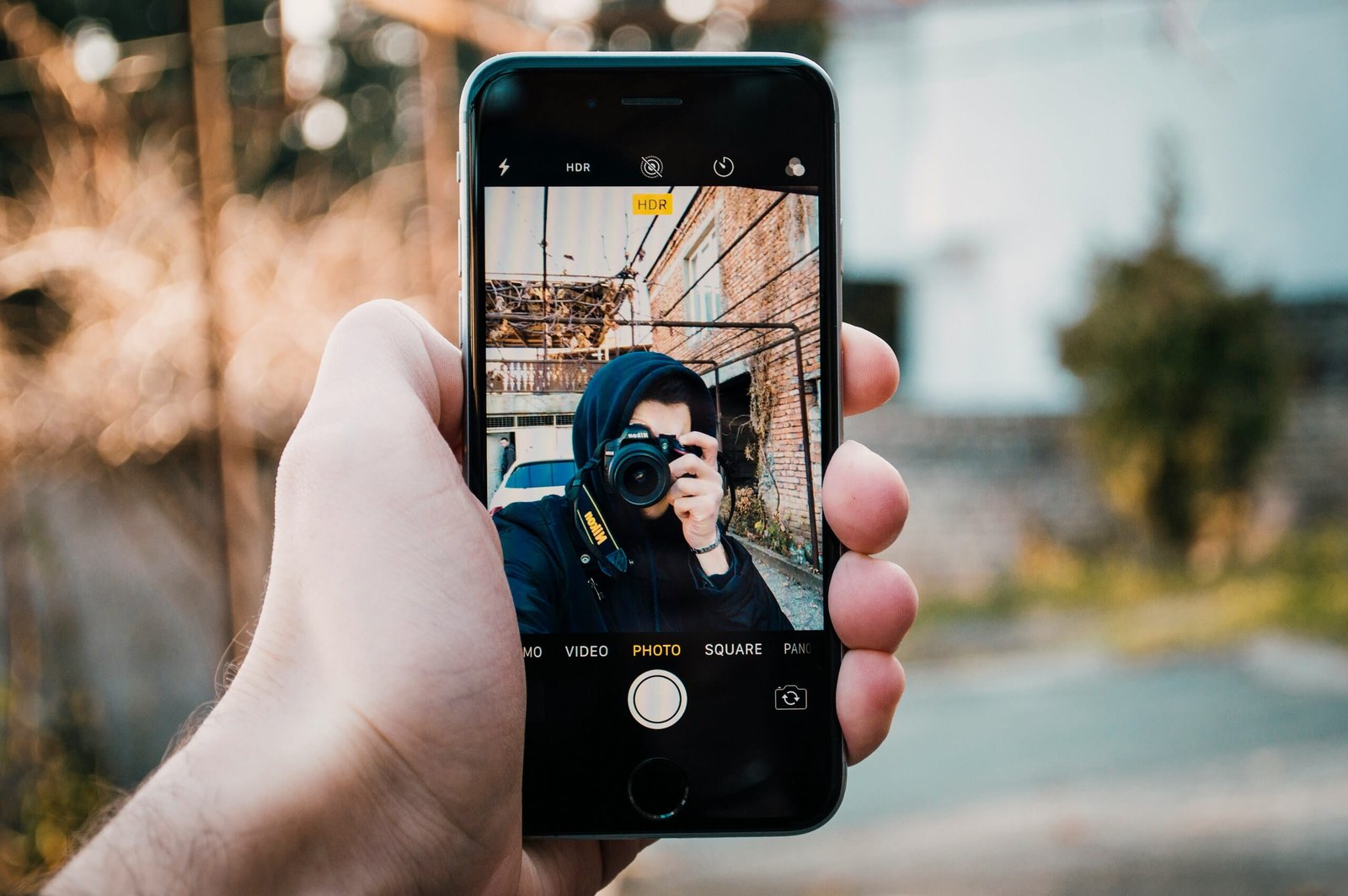 Mano con teléfono y app de cámara mostrando selfie con réflex, explorando ¿Qué ocurre después de hacer clic? en fotografía.