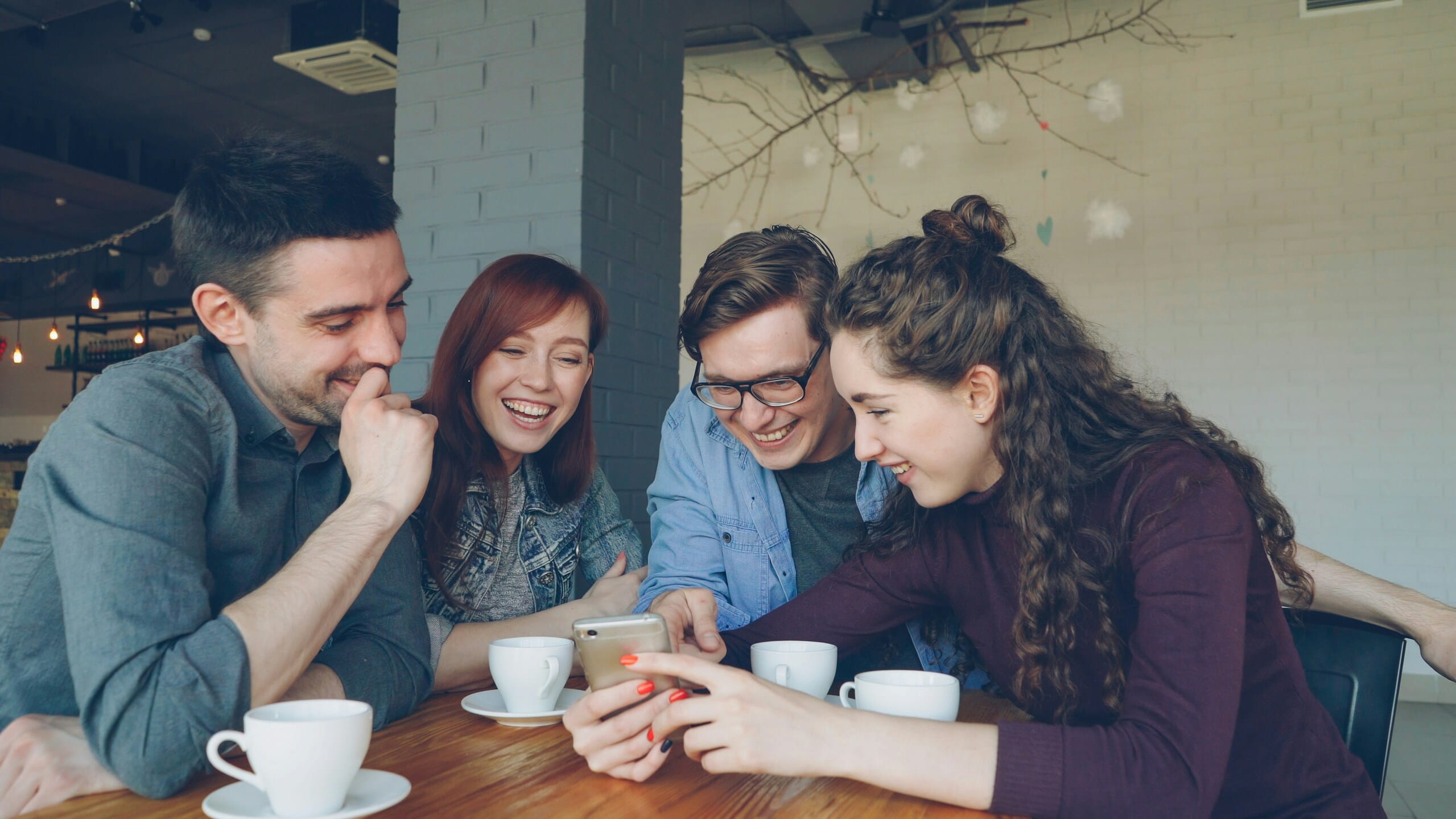 Cuatro jóvenes ríen alrededor de un móvil en una cafetería, un momento de Storytelling emocional que une emoción, memoria y decisión.