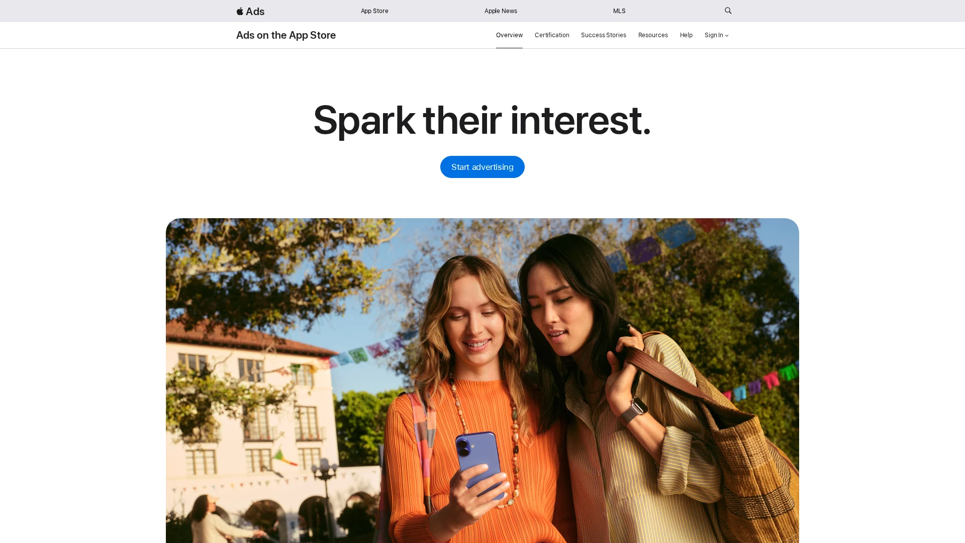 Dos mujeres mirando un smartphone al aire libre bajo la luz intensa del sol, como ilustración de una campaña publicitaria de Apple Ads.